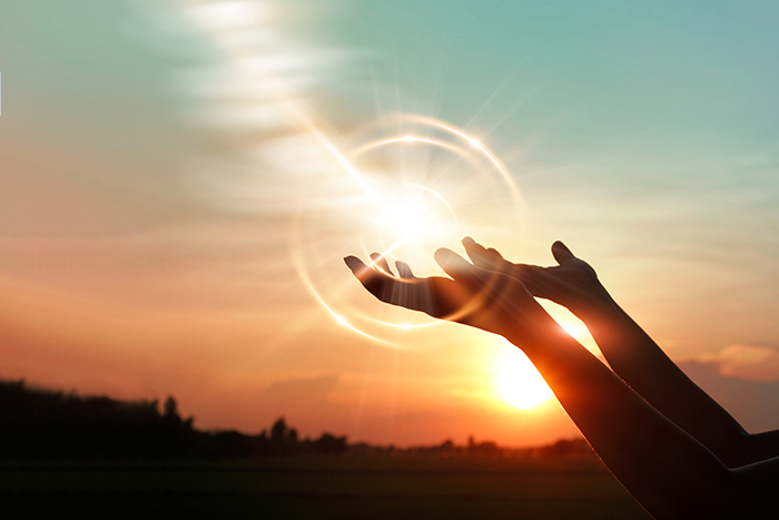 an image of two hands held up high with the sun coming through them